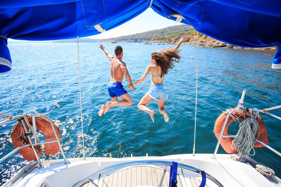 A couple holding hands jumps off the back of a boat into the blue water of Lake Texoma